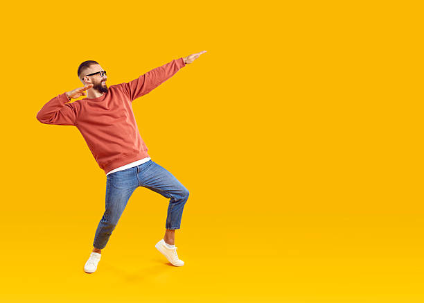 istock Cheerful man having fun showing dance moves in dab style on orange background in studio. 2212535148