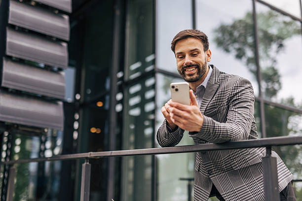 istock Smiling businessman using smartphone leaning on railing in urban setting 2212535180