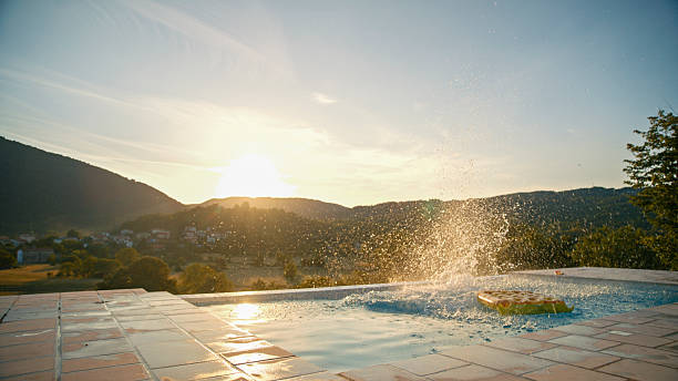 Itaipava, Rio de Janeiro, Brazil - October 2, 2019: A poolside retreat set against the backdrop of rolling green hills and a clear blue sky in Brazil. The sun shines brightly, illuminating the stone-paved patio, lounge chairs, and surrounding lush tropical vegetation.