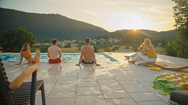 Itaipava, Rio de Janeiro, Brazil - October 2, 2019: A poolside retreat set against the backdrop of rolling green hills and a clear blue sky in Brazil. The sun shines brightly, illuminating the stone-paved patio, lounge chairs, and surrounding lush tropical vegetation.