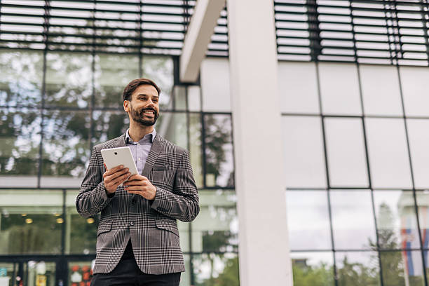 istock Smiling businessman holding digital tablet outside office building 2212535560