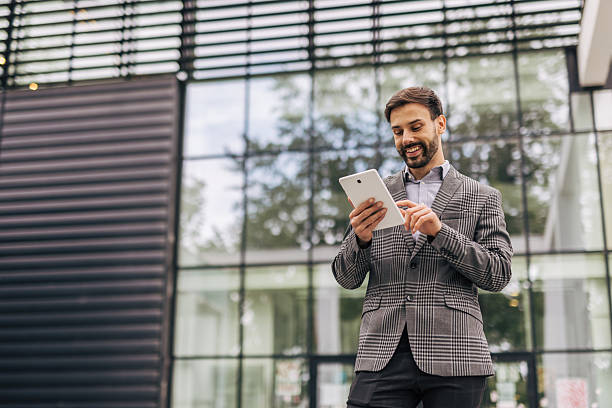 istock Smiling businessman using digital tablet in front of office building 2212535627
