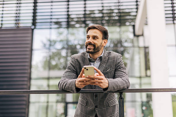 istock Smiling businessman leaning on railing and using smartphone 2212535786