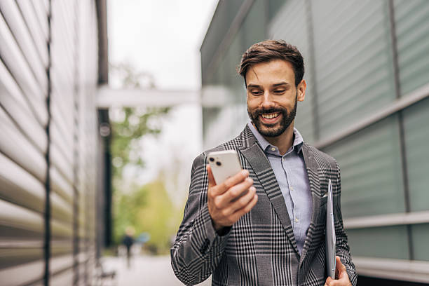 istock Smiling businessman using smartphone walking near office building 2212536233