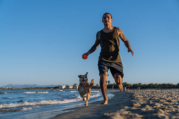 istock Young man running with dog on the beach 2212536584