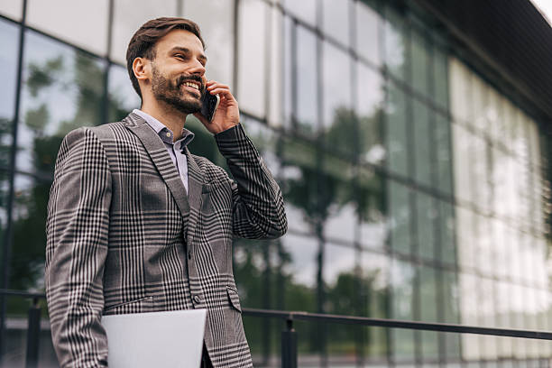 istock Businessman smiling while talking on phone in front of office building 2212536613
