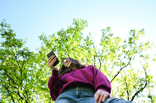 Young woman using smartphone under green tree canopy