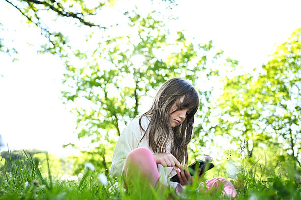 Girl using smartphone sitting in grass in park during springtime