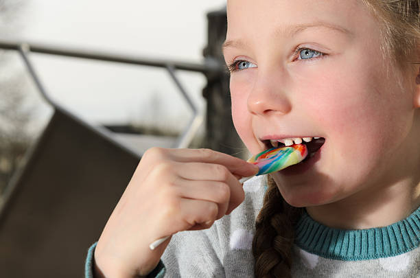 istock A girl with loose milk teeth is biting a candy. 2212541658
