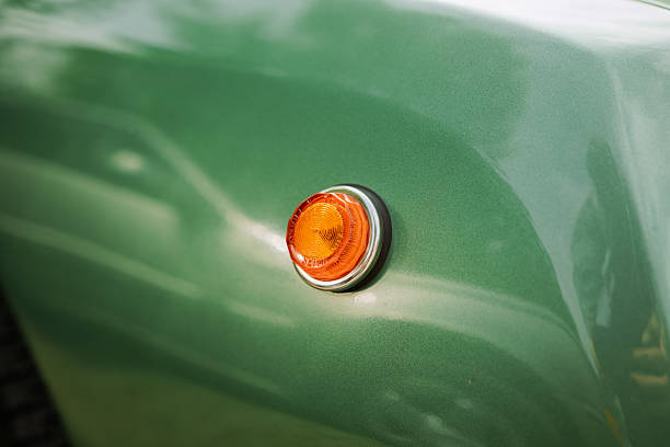 A close-up of a green vintage car’s rear section showcasing its angular tail light and glossy bodywork. The bright, reflective surface and clean lines highlight the precision and style of classic automotive design. The blurred background adds depth and enhances the retro aesthetic.