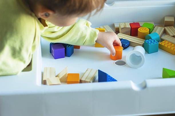 istock A small child plays with geometric wooden colored figures on a children's table 2212548475