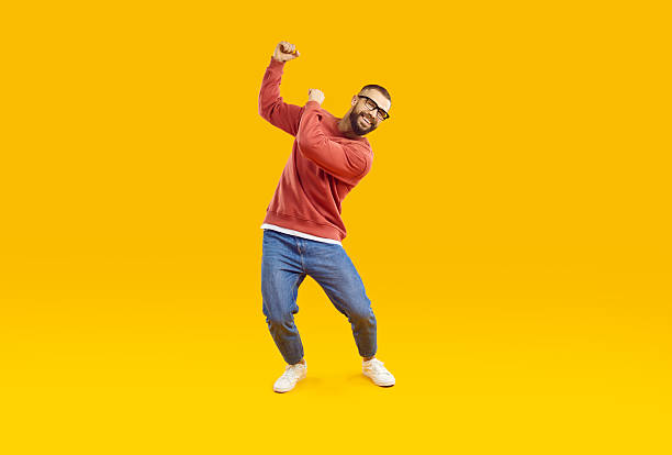 istock Cheerful, joyful and carefree man is having fun dancing on orange background in studio. 2212558659