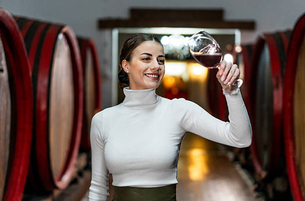 istock Woman examining wine in cellar with oak barrels 2212558870