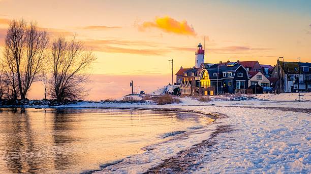 istock Tranquil winter sunset at a coastal village with a lighthouse and serene water reflections 2212559680