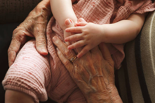 A cropped image of a great grandmother holding her five month old great granddaughter's hands as she sleeps on her lap. Shot with a Canon 5D Mark IV.