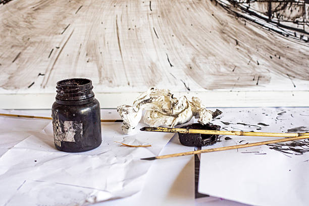 Array of paintbrushes of different sizes and colors alongside cans of acrylic paint with visible colors isolated on a white background