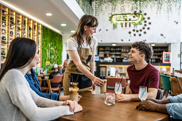 istock Young waitress serving drinks to happy customers at a modern cafe 2212566663
