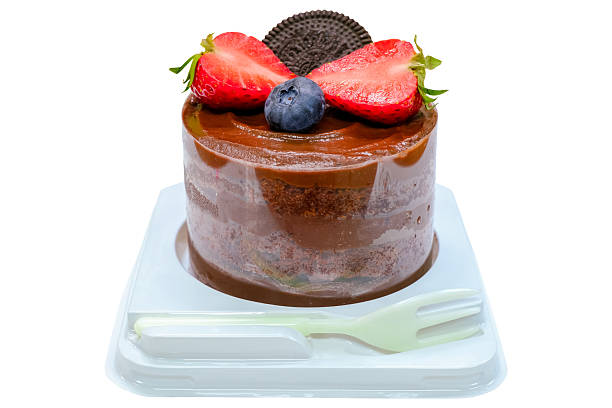 Delicious sweet chocolate cake topped with fresh strawberries, a blueberry, and a cookie, served in a plastic container with a plastic fork. isolated on white background with clipping path