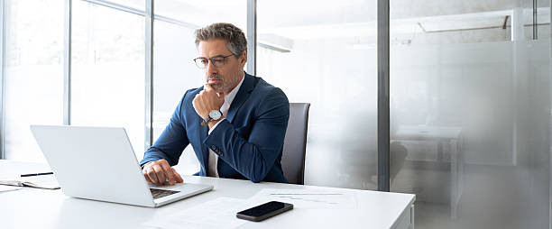 istock Focused latin senior in suit financial expert analyst thinking on sale solution. Professional indian manager investor using pc laptop computer sitting at desk workplace in office. Banner, copy space 2212567024