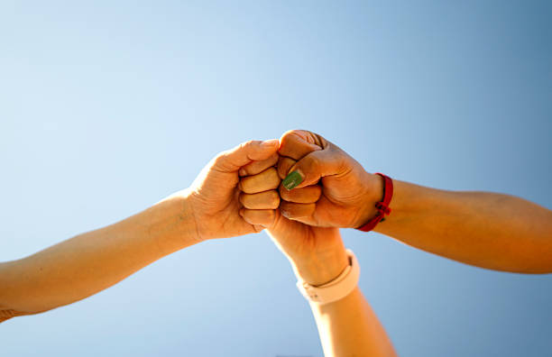 istock Three people showing teamwork and collaboration by bumping their fists together against blue sky 2212567871