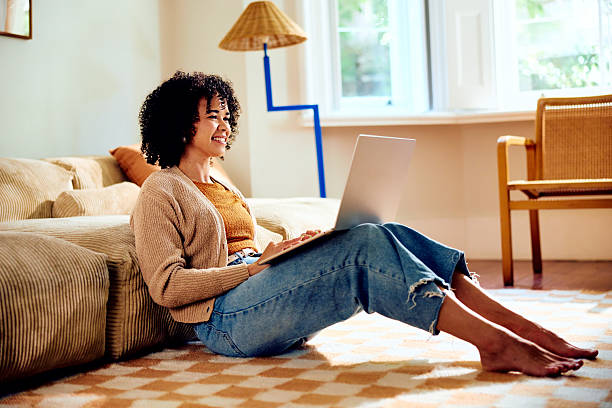 istock Young woman sitting on floor using laptop, working from home, smiling 2212569380