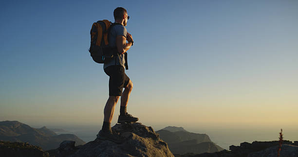 istock Back, man and hiker with backpack or mountain view for hiking adventure or conquer on rock. Male person, tourist or explorer with bag on cliff or peak for trekking journey or trip on space in sunset 2212569711