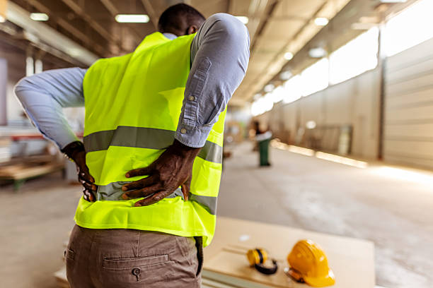 Worker Wearing Safety Gear Experiencing Back Pain in a Factory Setting