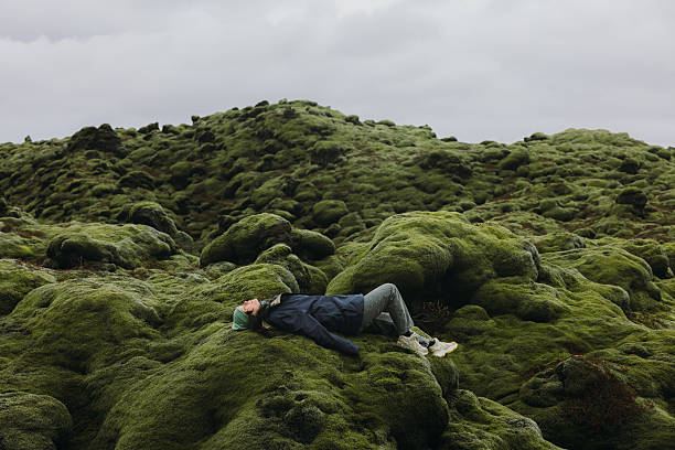 Female lying in tranquility on endless green volcanic landscape covered by soft moss in Iceland
