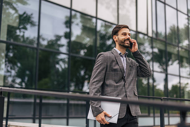 istock Businessman walking and talking on phone outside office 2212573982