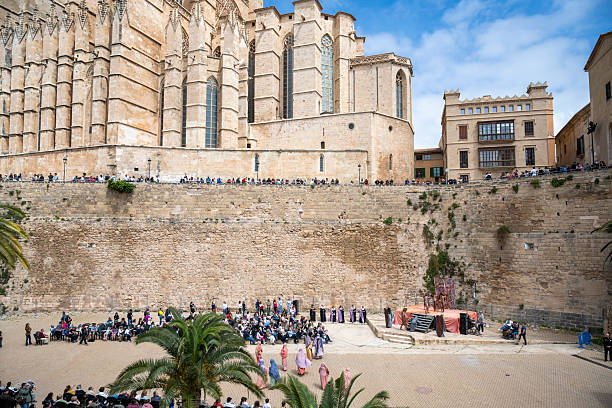 18 April 2025 Palma de Mallorca, Spain. Performers in traditional costumes stage a Good Friday Passion play at the foot of La Seu Cathedral, as crowds gather on the ancient walls and square to watch the solemn event under the spring sky.