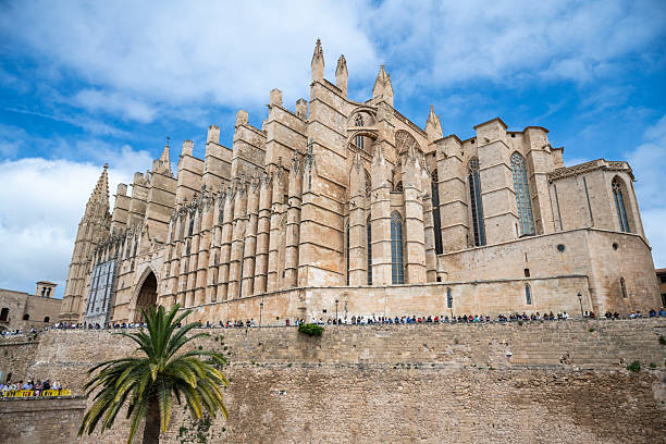 18 April 2025 Palma de Mallorca, Spain. People line the ancient walls of La Seu Cathedral in Palma, Mallorca, gathering for the traditional Good Friday celebrations beneath a vibrant spring sky.