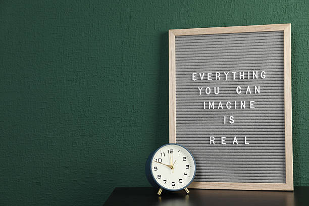 istock Letter board with phrase Everything You Can Imagine Is Real and alarm clock on table near green wall. Space for text 2212585615