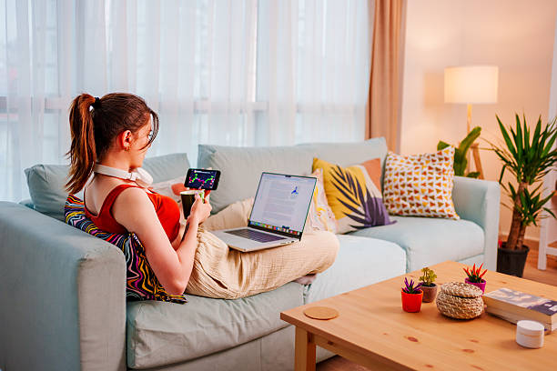 istock Focused young woman  sits on the couch analyzing financial data on laptop at home with headphones 2212588119