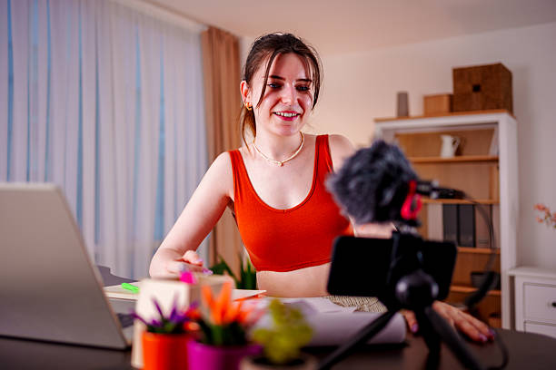 istock Young woman recording video content at home with smartphone and microphone setup 2212588152
