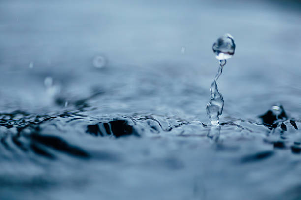 Water rain droplet forming splash crown in turquoise blue water in sparkling light