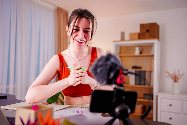 istock Young woman recording video content at home with smartphone and microphone setup 2212594711