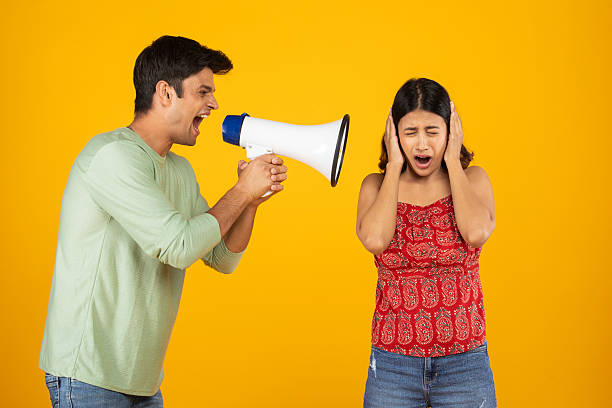 istock Man shouting with megaphone at his girlfriend on yellow background 2212599448
