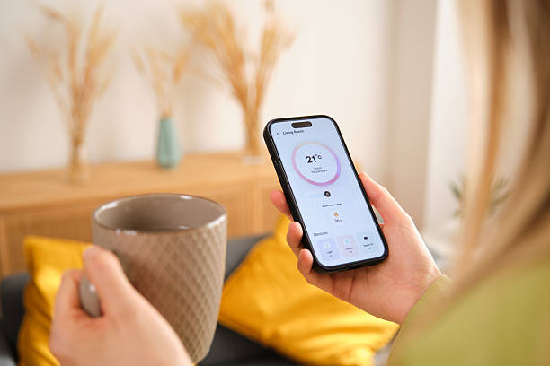 istock Woman using mobile app to control home temperature while enjoying a hot drink 2212599548