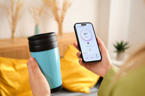 istock Woman managing smart home devices using a phone app, holding a thermal mug 2212599578