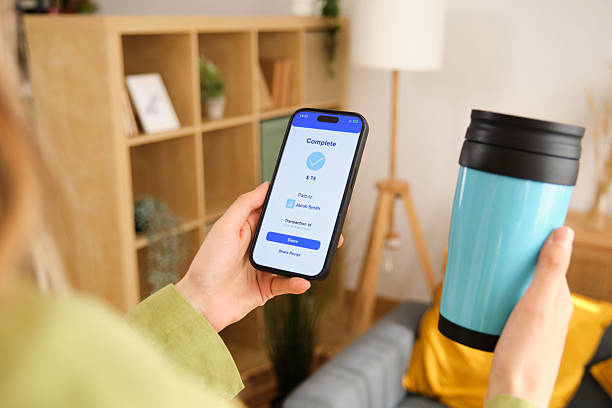 istock Woman paying for her reusable cup with mobile phone using online payment app 2212600397