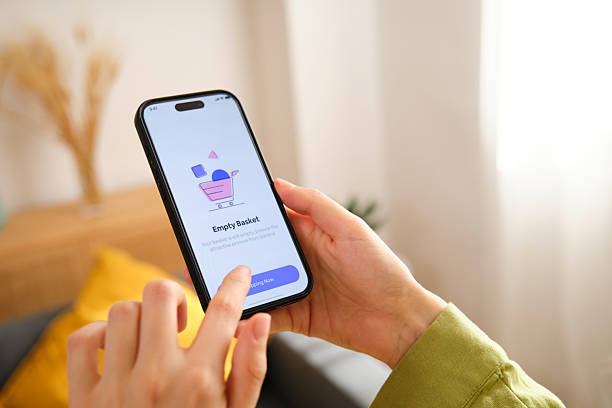istock Woman using smartphone with empty shopping basket app at home 2212600484