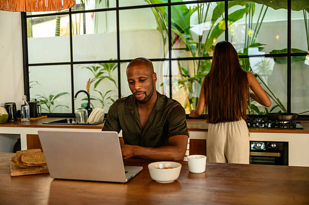 istock Man working on laptop while woman cooks in a modern kitchen environment 2212601757