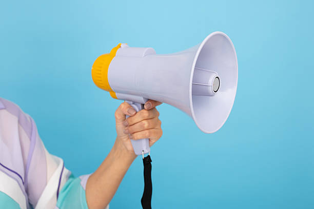 istock Woman shouting through megaphone against vibrant blue backdrop 2212604419