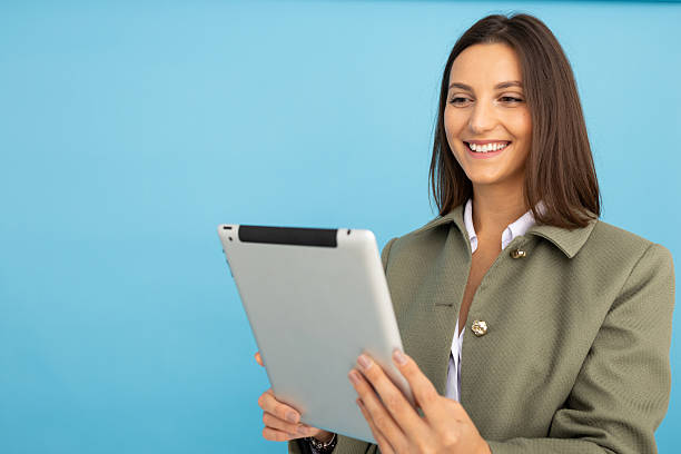 istock Professional woman smiling, working on digital tablet against blue backdrop 2212604595