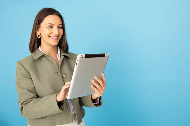 istock Young businesswoman using digital tablet and smiling on blue background 2212604602