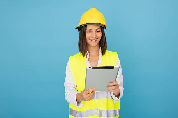 istock Young female architect wearing safety vest and helmet using digital tablet, isolated on blue background 2212607442