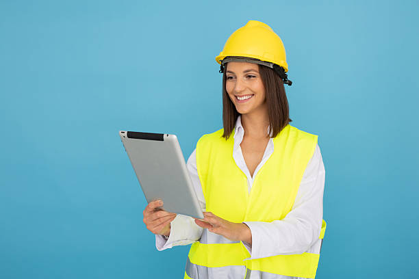 istock Female engineer wearing protective gear, holding digital tablet, smiling confidently against blue background 2212607469