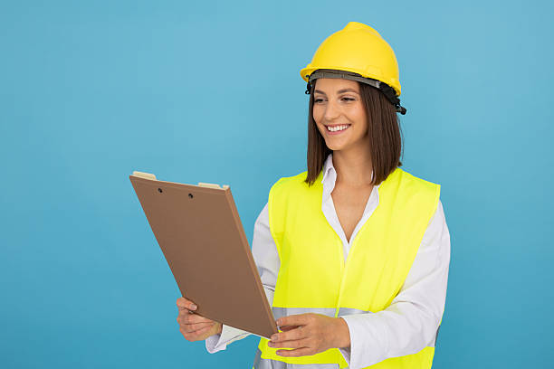 istock Female engineer wearing protective gear, reviewing project notes with confident smile, standing against blue backdrop 2212607609