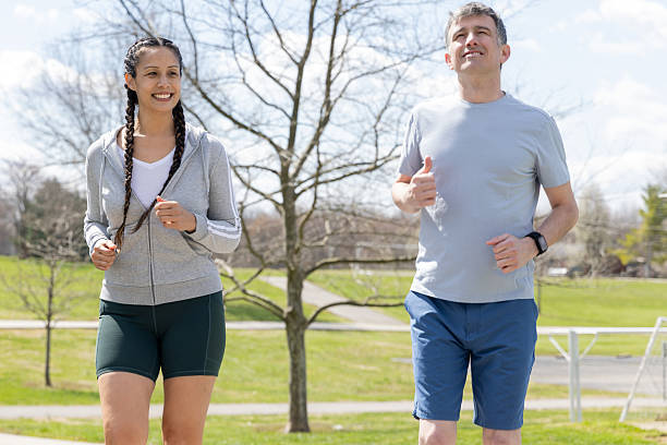 istock Smiling Couple Runs Side-by-Side Through Sunny Park 2212608407
