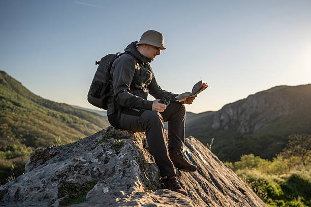 Male Explorer Sitting on Rock Reading a Map in Scenic Mountains